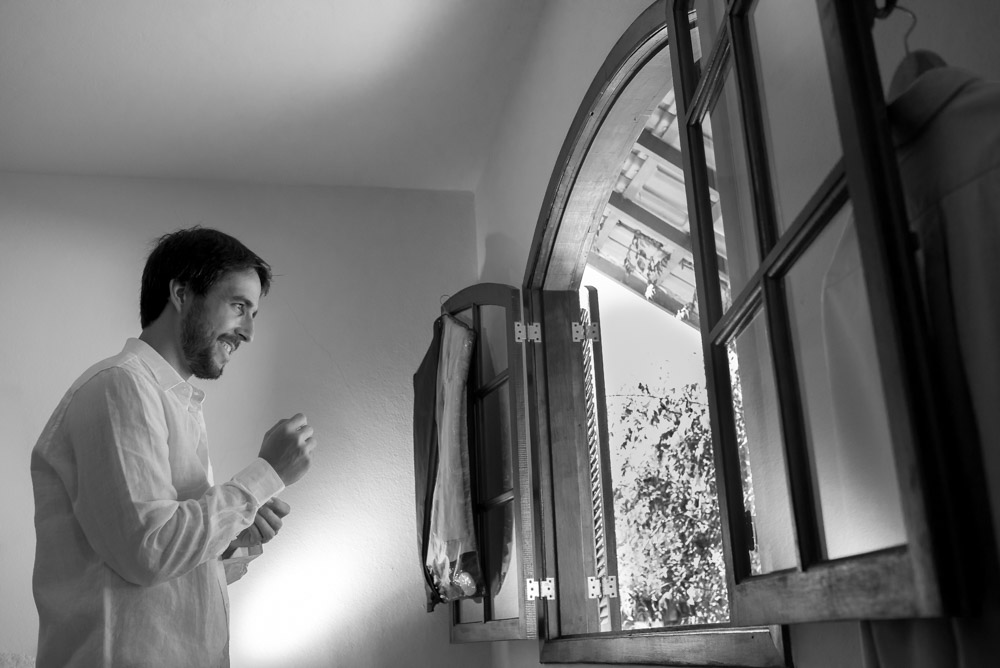 Image of a groom putting his shirt on and buttoning his sleeves in black and white