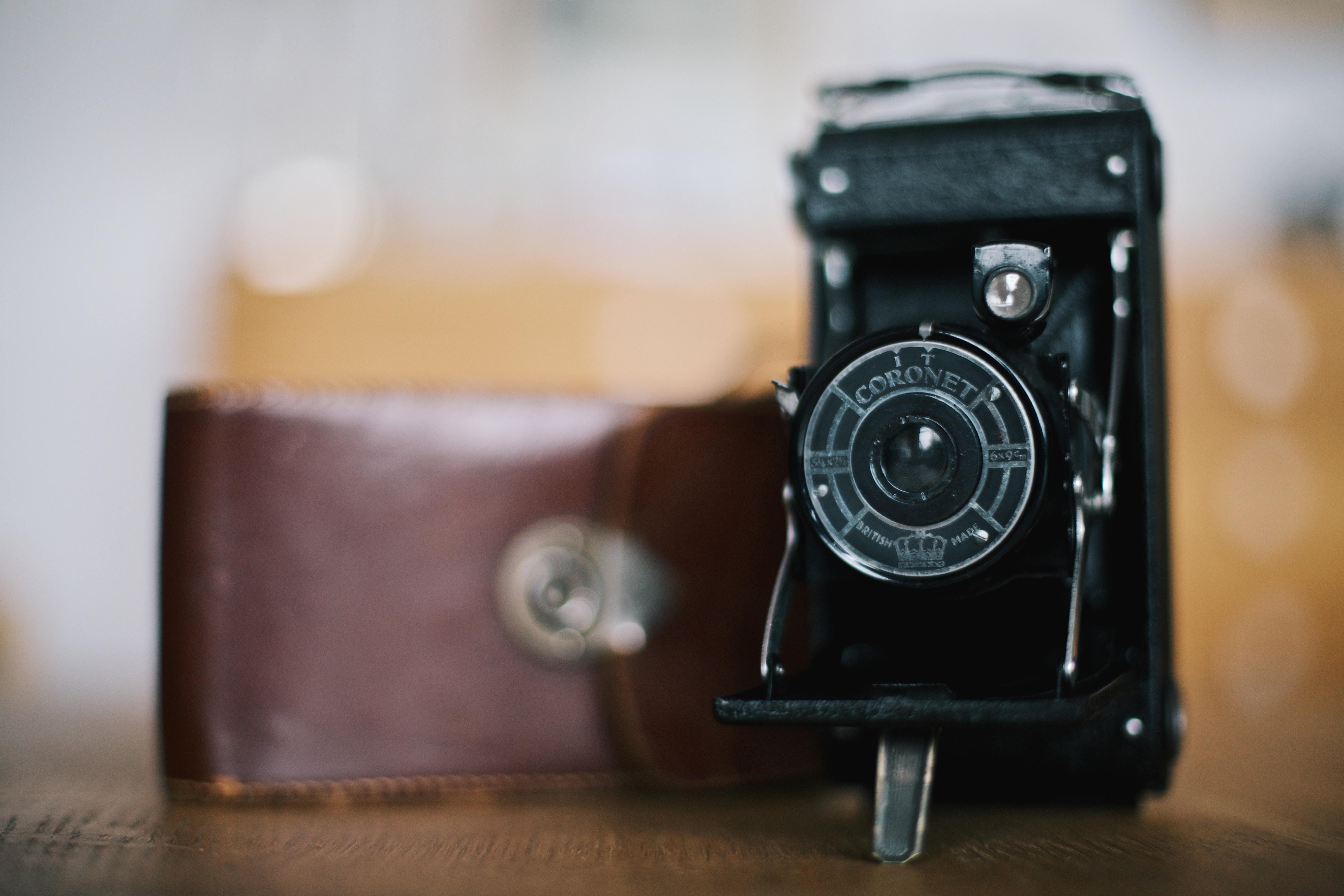 An old Coronet film camera and leather case on a wood table.