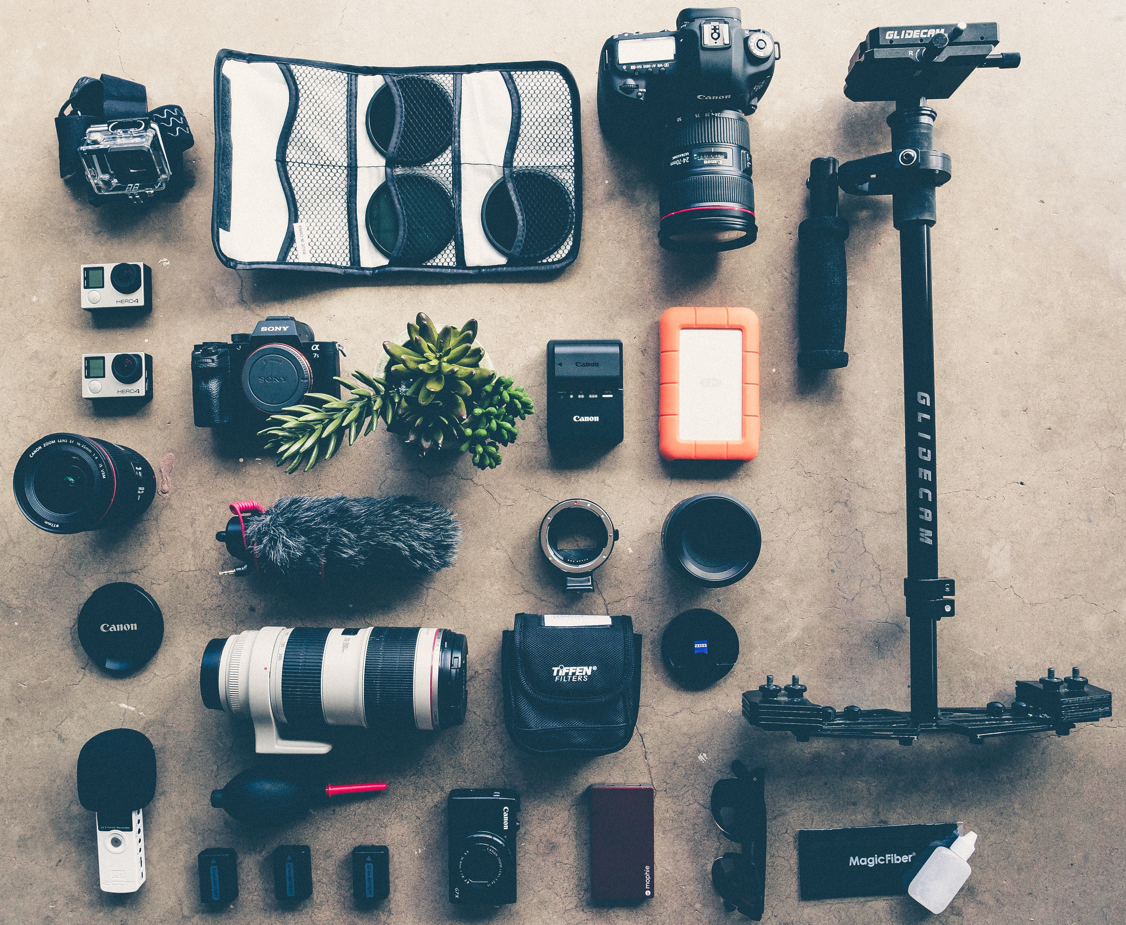 A collection of camera equipment - a Canon DSLR camera, a Sony mirrorless camera, a compact camera, several lenses, and more.