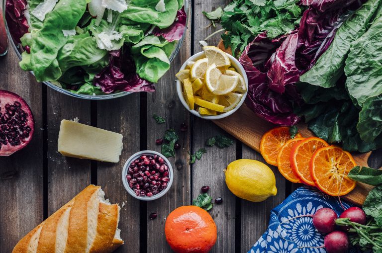 A salad, fruit, and bread on a wooden table.