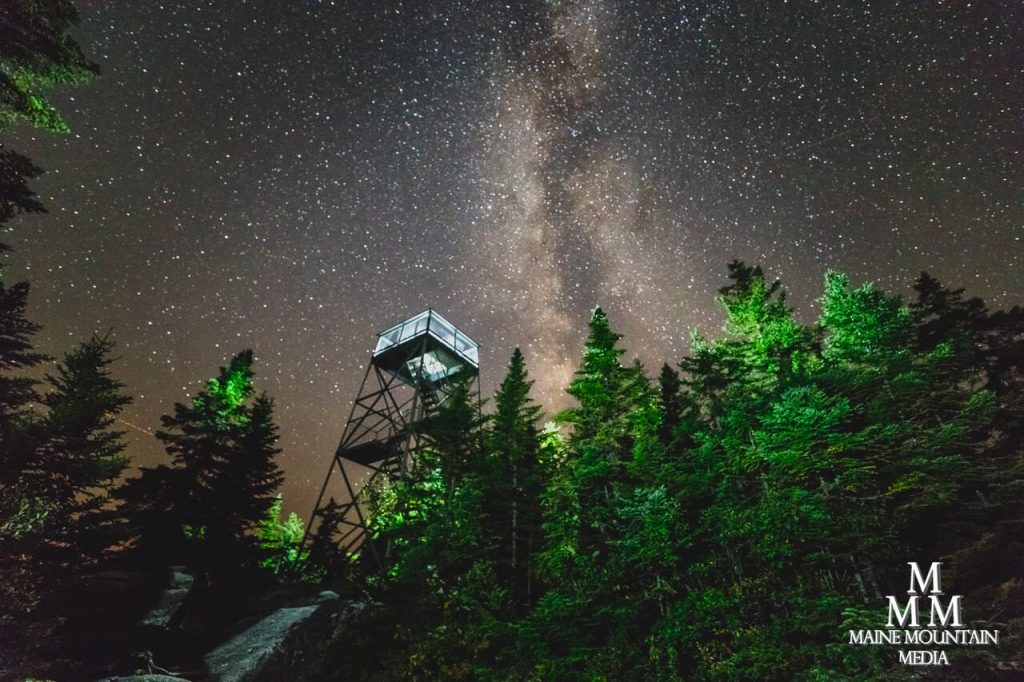 Example image of nightscape photography settings of a starry night sky and green fir trees on a cliff