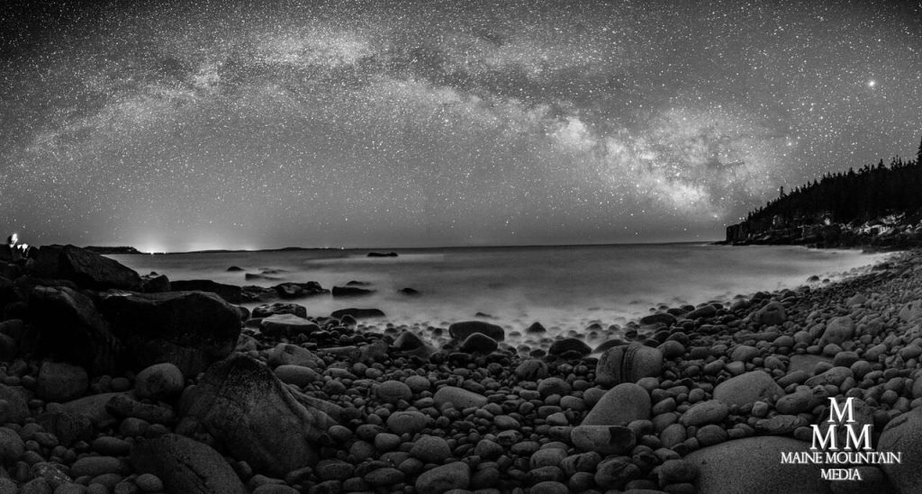 Black and white nightscape picture of a rocky beach with a starry sky
