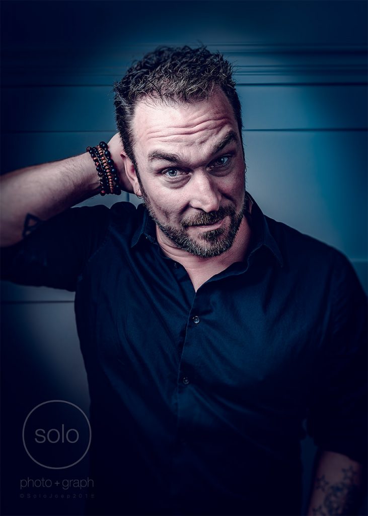 Example of creative portrait photography of a man in a dark button up shirt with his hand behind his head