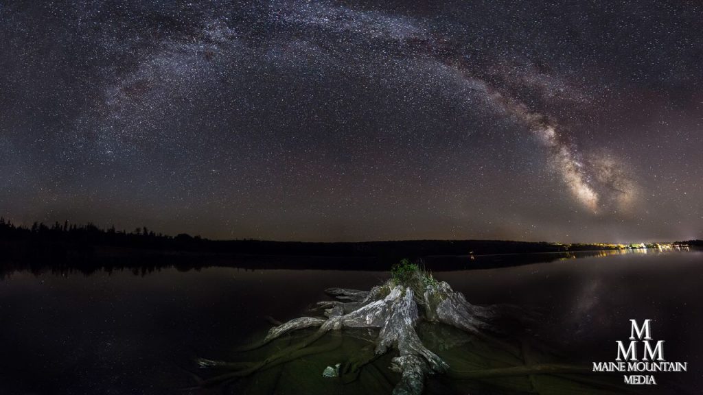 Nightscape image of a stump in a lake and a starry night sky