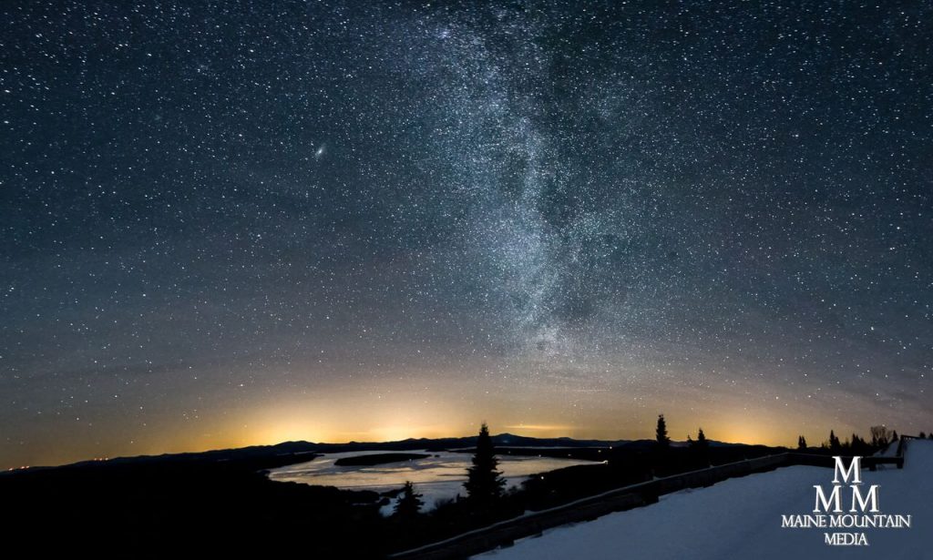 Picture of a starry night sky overlooking a river and with snow on the ground