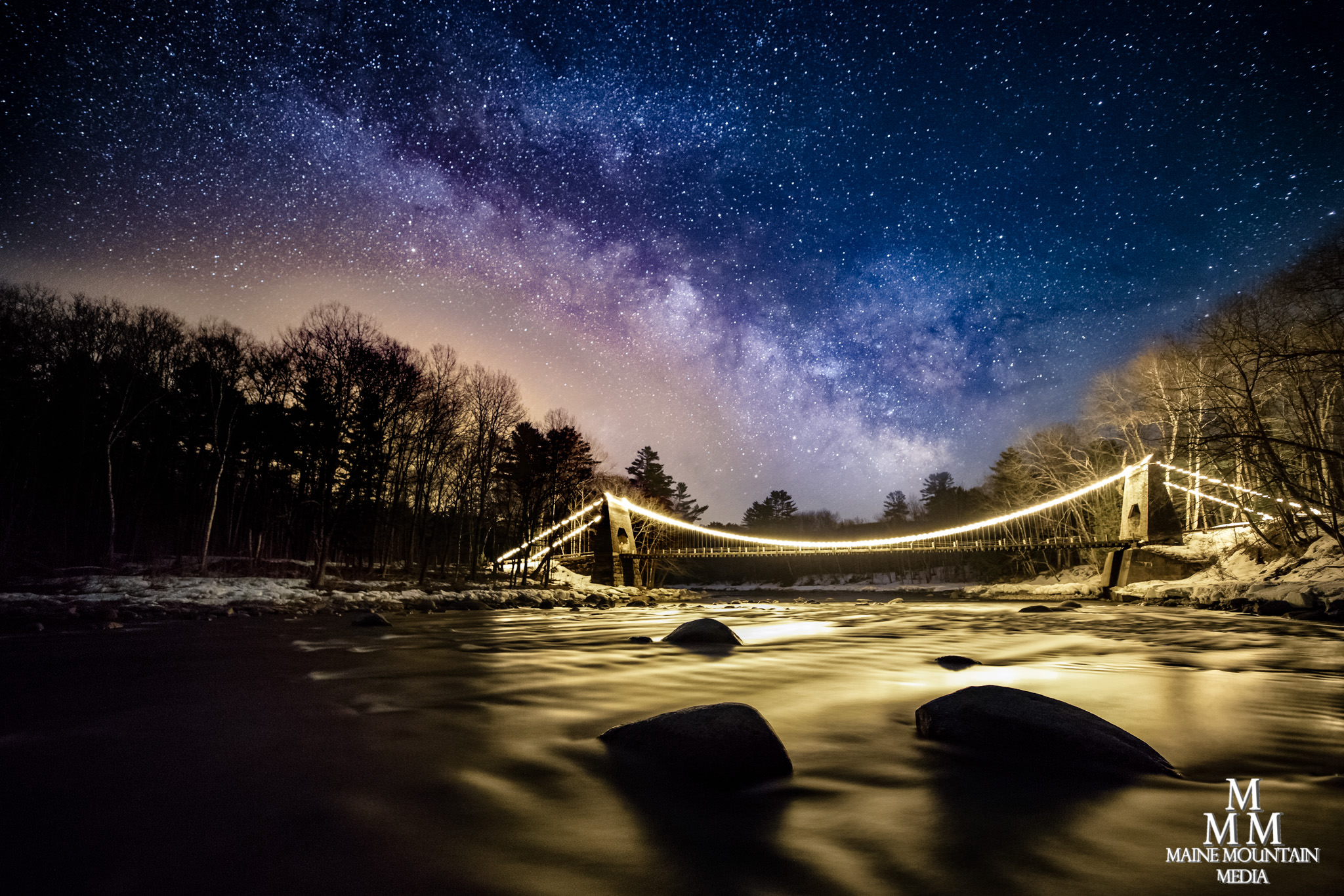 A river with a lit-up bridge and the Milky Way in the background.