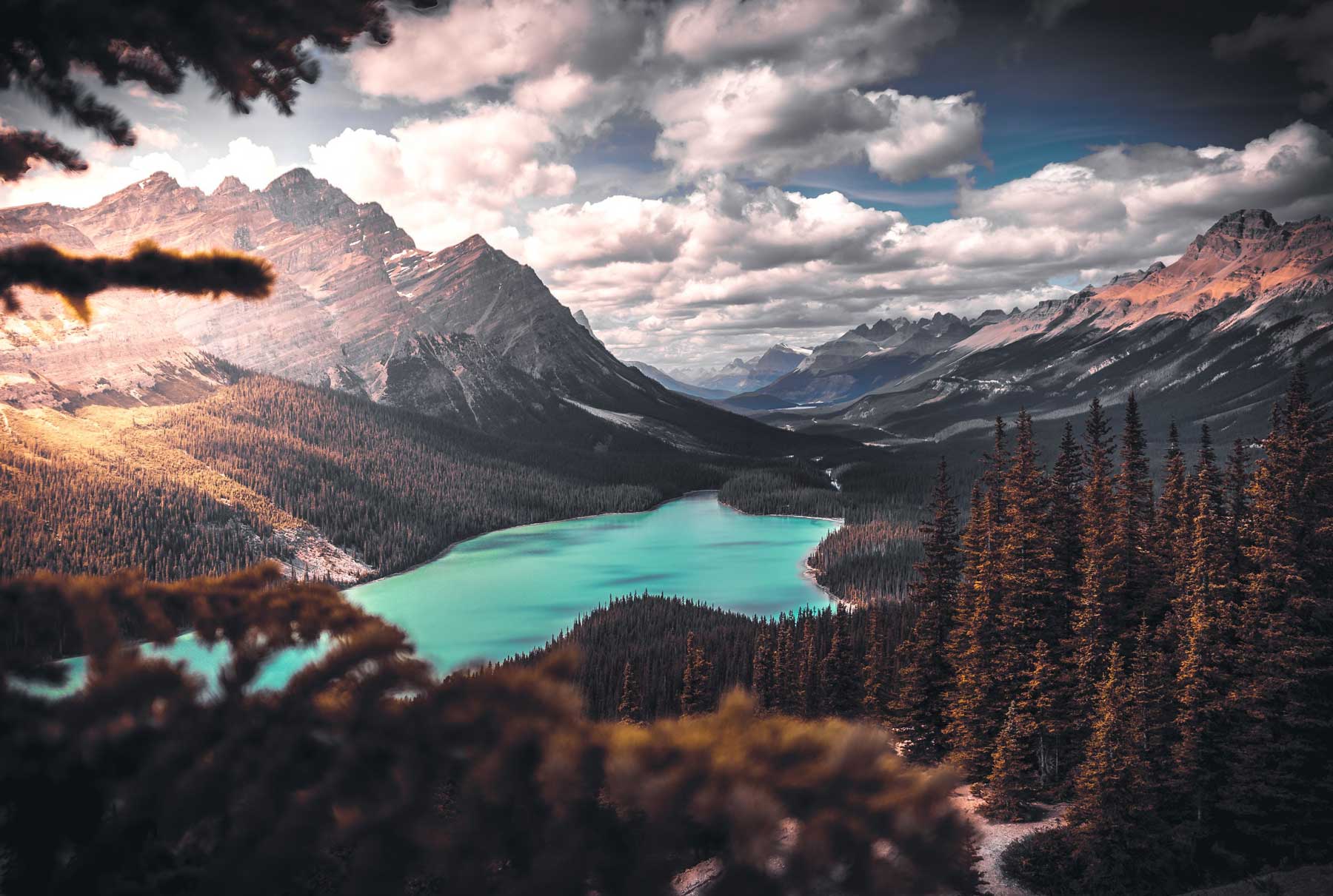 A landscape with mountains and a blue lake with the sun shining through clouds.