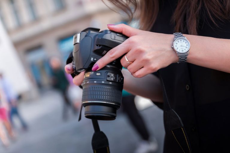 A person holding a DSLR camera with a zoom lens on a street.