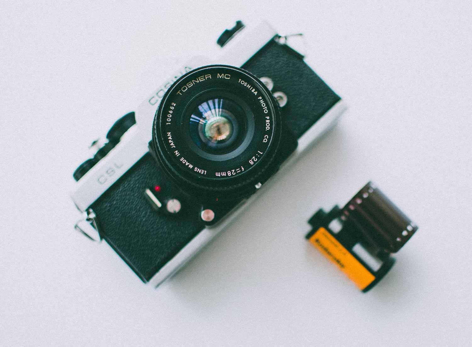 A silver film camera and a film canister on a white surface.