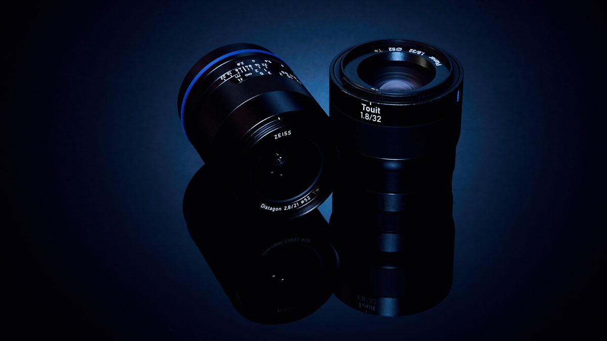 Two Zeiss camera lenses on a black shiny surface.