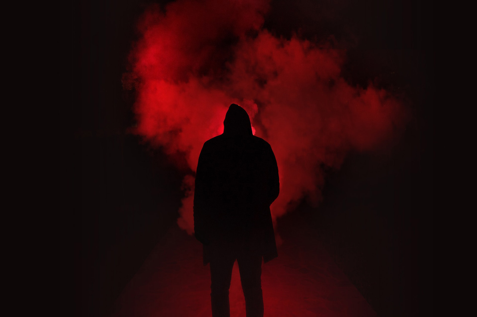 A man's silhouette in a red dark scene with smoke/fog.