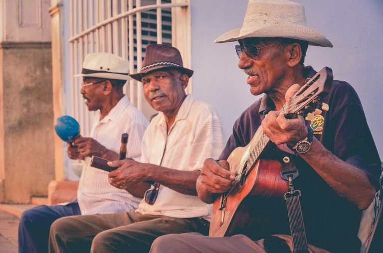 Three latino men with hats on playing music.