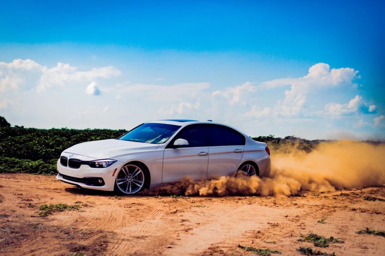 A car peeling out on a dirt road kicking up dirt.