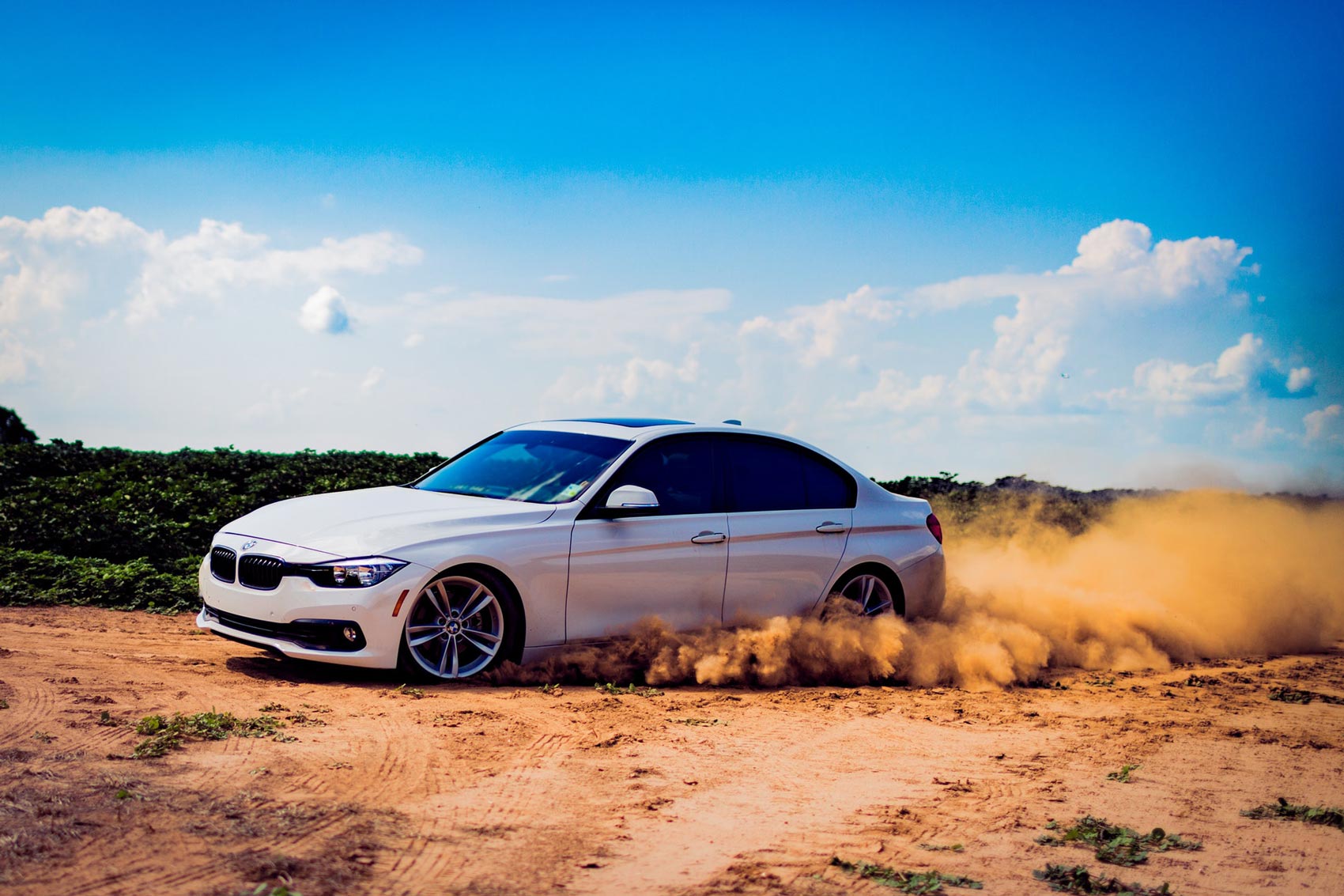 A car peeling out on a dirt road kicking up dirt.
