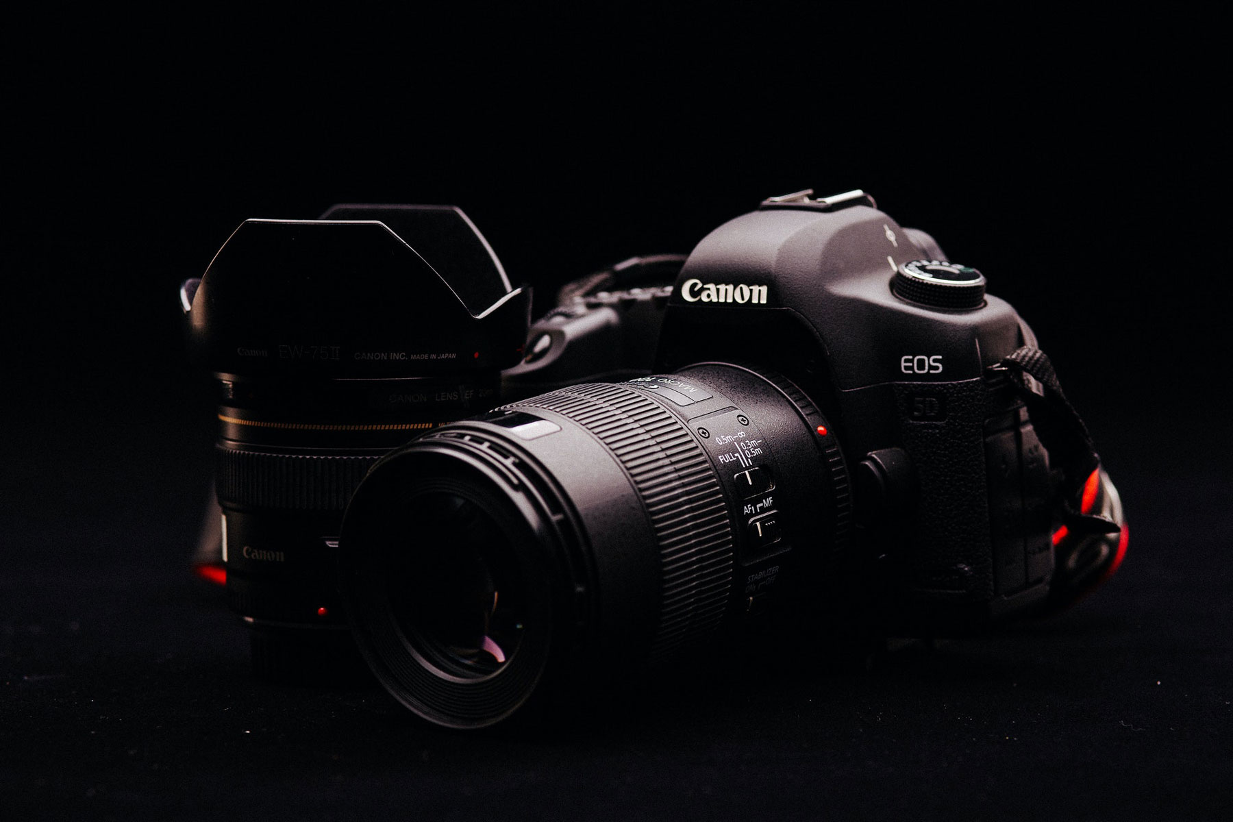 A black Canon camera and lenses against a black backdrop.