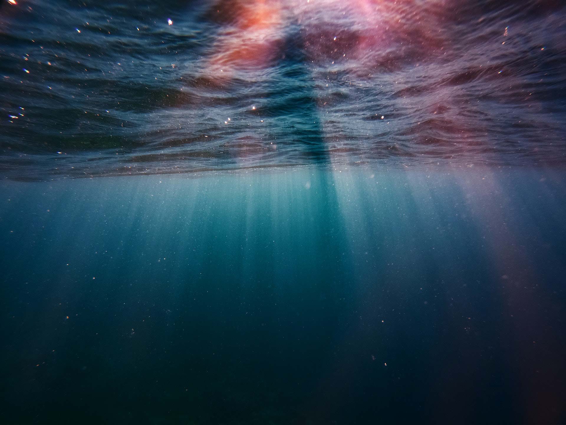 Underwater looking up with colorful light coming down into the water.