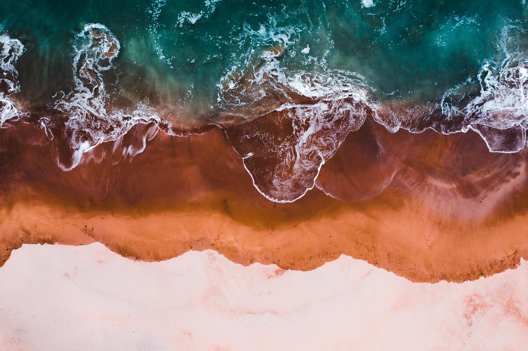A beach with blue and green waves crashing to shore from above.