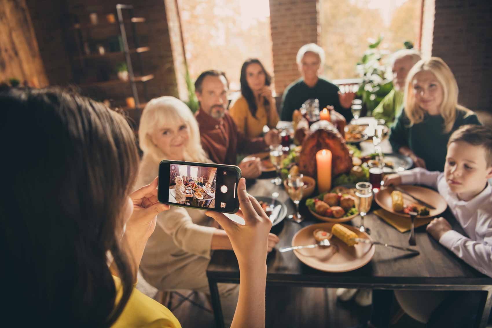 A woman photographing a family at Thanksgiving dinner on her phone