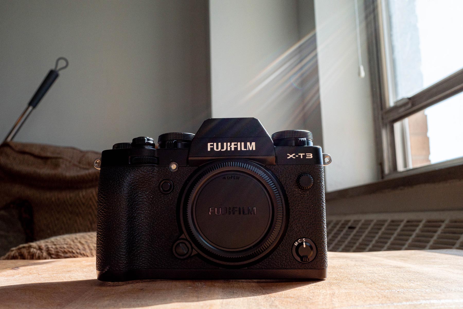 The Fujifilm X-T3 on a wood table next to a window with sunlight coming in.