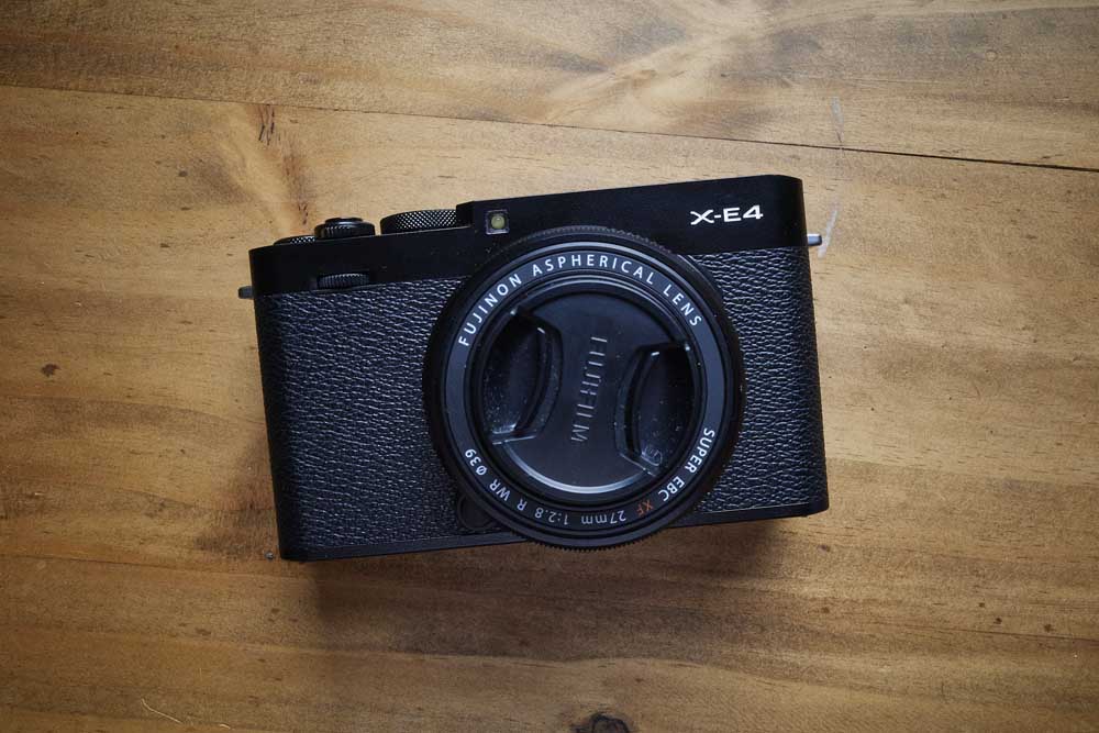 The Fujifilm X-E4 on a wood table from above.