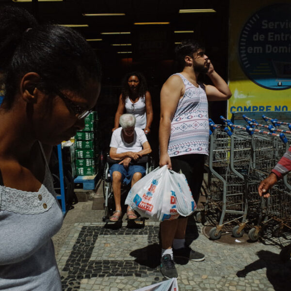 A woman looking down in front of a market. There's a man holding a phone and two women exiting, one in a wheelchair.