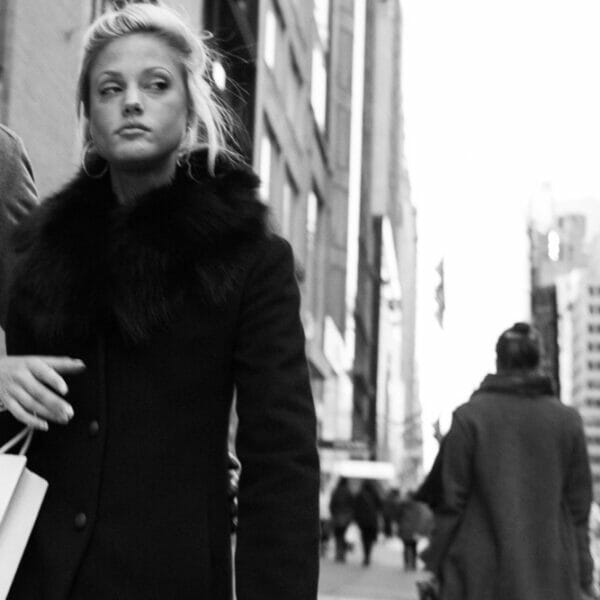 Blonde woman walking down sidewalk carrying Dior bag hand in hand with a man.