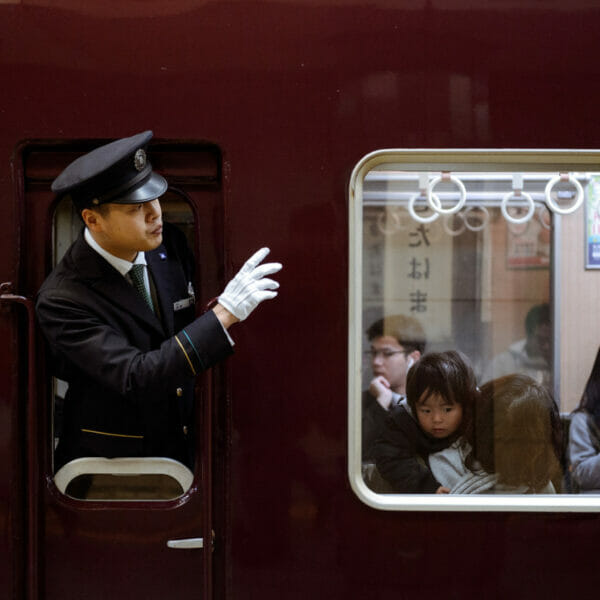A train conductor looking out of window and passengers.