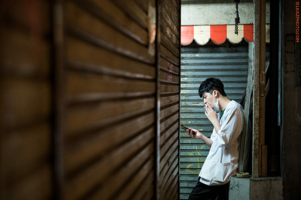 A man smoking a cigarette in a back alley in Japan.