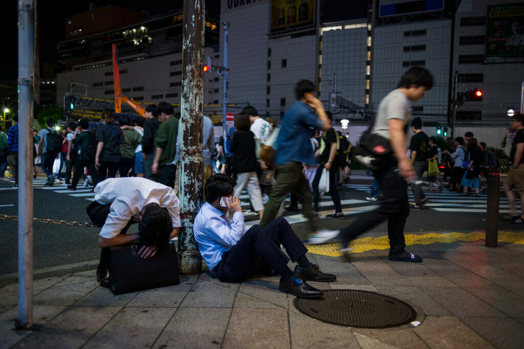 Two businessmen sitting on a sidewalk on a busy street.