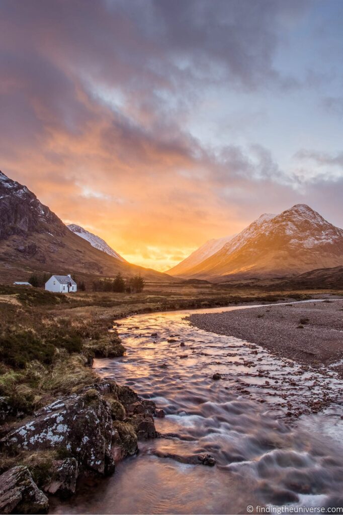 A creek in front of mountains at sunset.