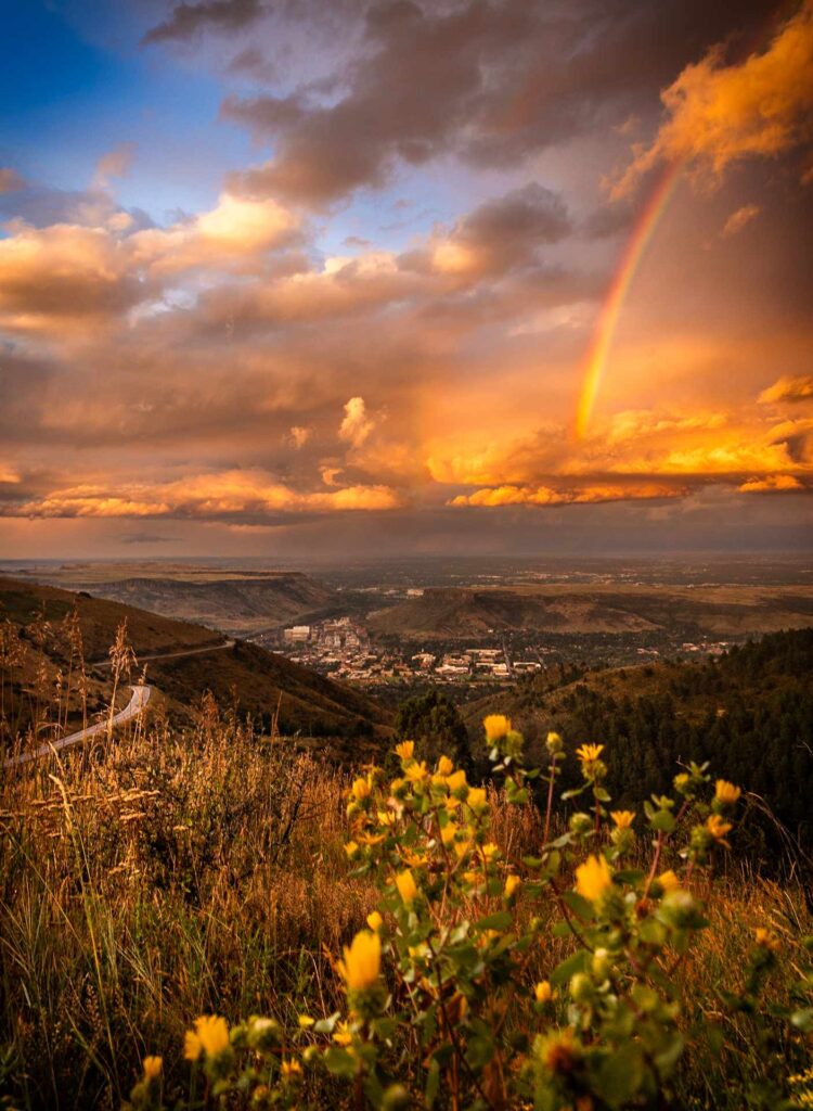 A view from a mountain looking down on a small town with a rainbow in the sky.