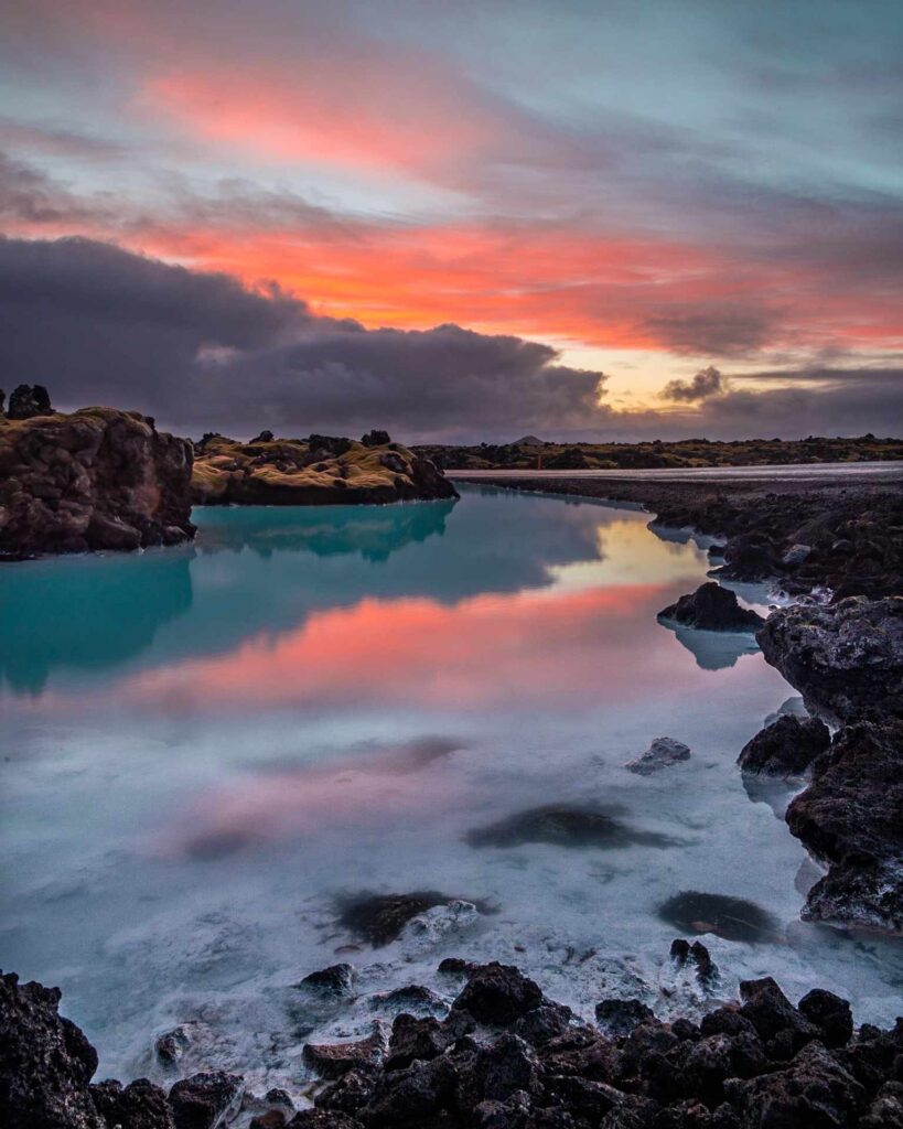 A turquoise blue rocky lake and a pink sky.